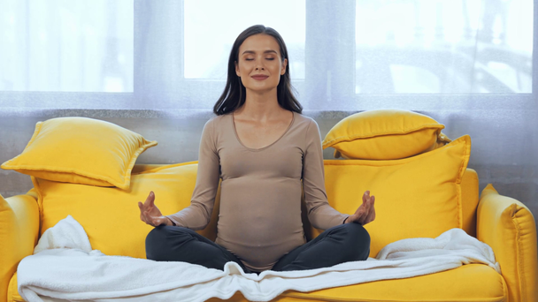 Mujer embarazada meditando en el sofá en casa - Imágenes, Vídeo