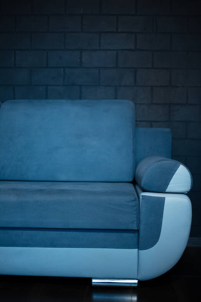 Close-up de parte do sofá azul no fundo da parede de tijolo preto. - Foto, Imagem