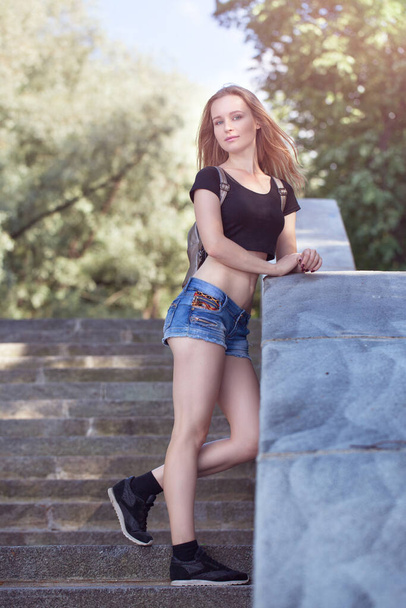 Young blond girl, in short shorts standing on the stairs - Φωτογραφία, εικόνα