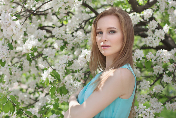 portrait of a young blonde girl in a blue dress. apple trees in flowers. - 写真・画像