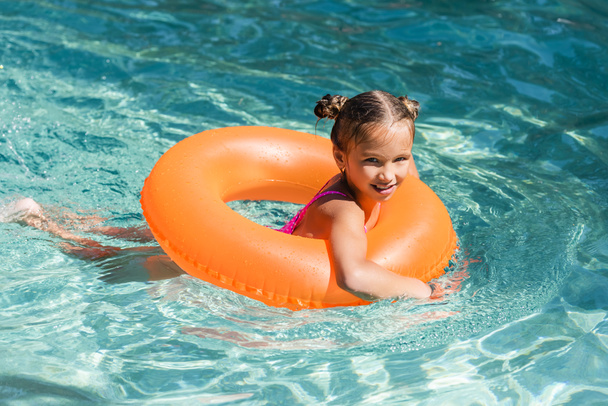 child looking at camera while floating in pool on swim ring - Foto, imagen