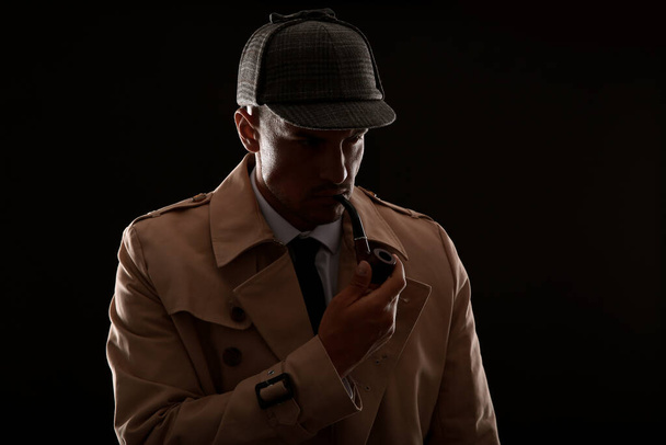 Old fashioned detective with smoking pipe on dark background - Фото, изображение