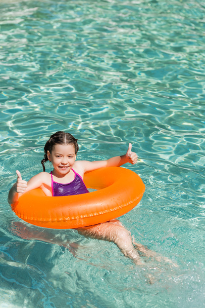 水泳の輪に乗ってプールに浮かんでいる間に親指を立てる楽しい子 - 写真・画像