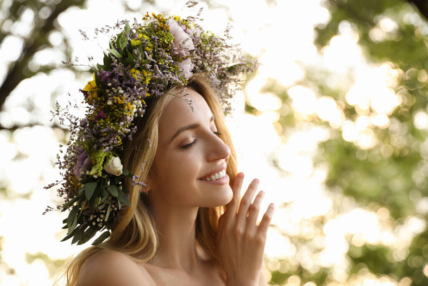 Young woman wearing wreath made of beautiful flowers outdoors on sunny day - Fotoğraf, Görsel