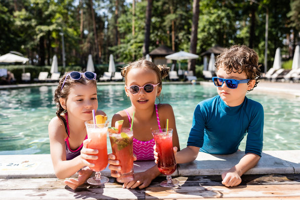 friends in swimwear clinking glasses with fresh fruit cocktails near pool - Фото, зображення