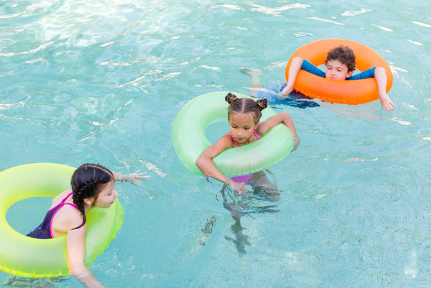 vista ad alto angolo di tre amici galleggianti in piscina su anelli di nuoto colorati - Foto, immagini