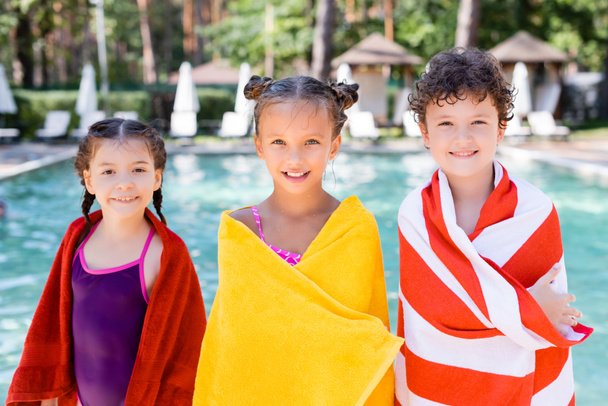 wet friends looking at camera while wrapping in terry towels near swimming pool - Photo, Image