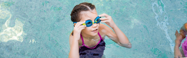 vízszintes kép a lány medencében megható úszószemüveg, miközben félrenéz - Fotó, kép