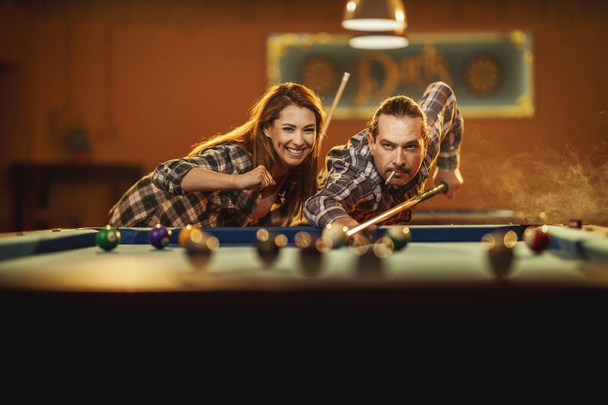 Joven sonriente pareja alegre está jugando al billar en el bar después del trabajo. Participan en actividades recreativas. - Foto, imagen