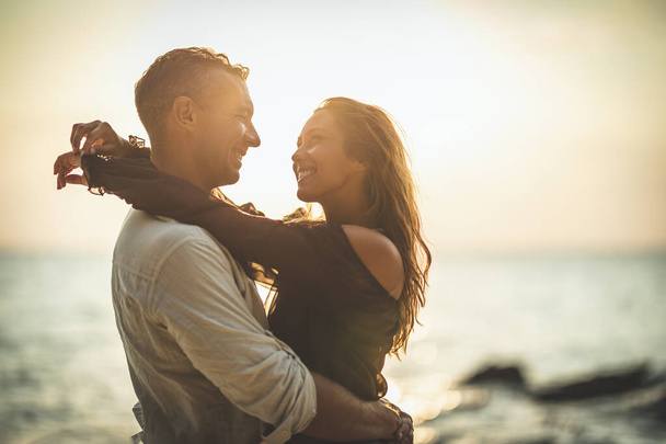 Un couple amoureux s'amuse et se promène sur la plage de sable vide au coucher du soleil. Ils se regardent.. - Photo, image