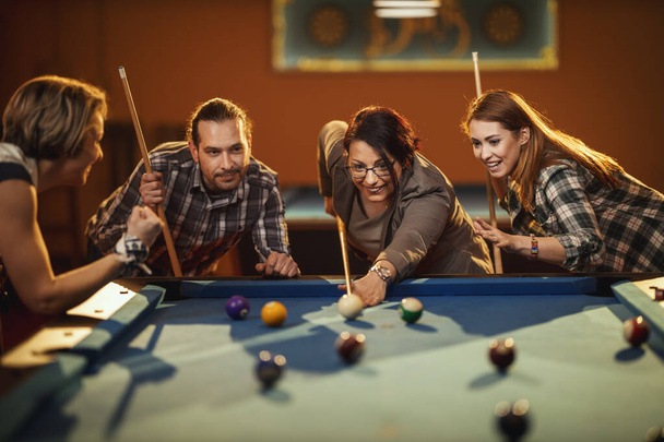 Jóvenes amigos sonrientes y alegres están jugando billar en el bar después del trabajo. Participan en actividades recreativas. - Foto, Imagen