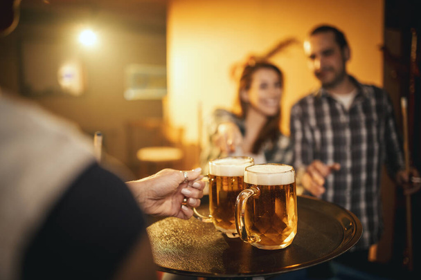 A pincérnő, aki sört szolgál fel a mosolygó, vidám párnak, biliárdozik munka után a bárban.. - Fotó, kép