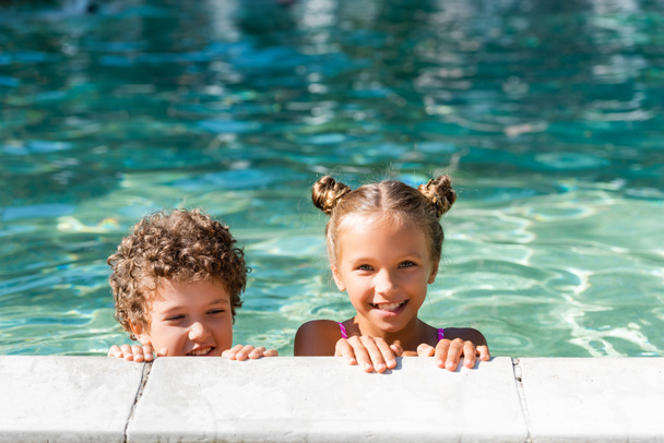 meisje op zoek naar camera terwijl het doorbrengen van tijd in zwembad met krullend jongen - Foto, afbeelding