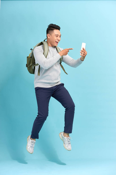Full length of handsome  young man taking phone while jumping against blue background. - Photo, Image