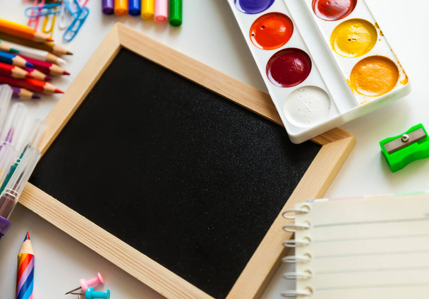 Blackboard in wooden frame surrounded by office and school supplies. Office and student gear over white background - Back to school concept - 写真・画像