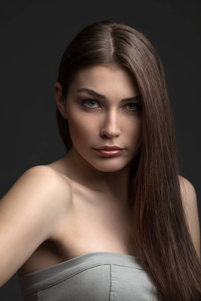 the beautiful girl poses in studio on a gray background. fashion portrait. make-up. long hair. - Fotó, kép