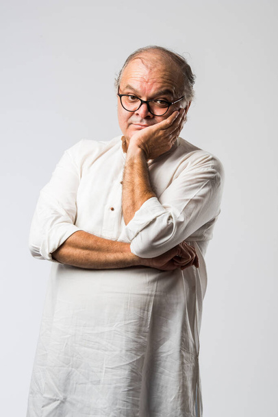 Portrait of cheerful Indian retired old man wears white kurta, pointing or presenting or in hands folded pose - Foto, afbeelding
