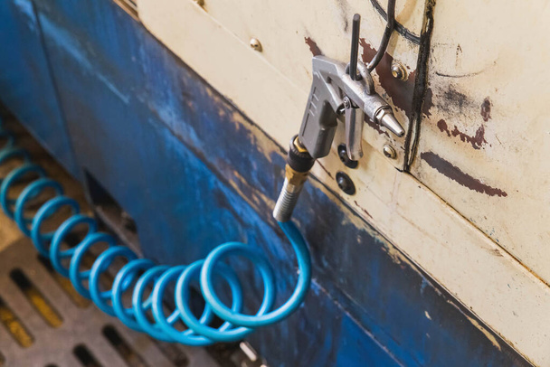 pistolet à air avec tuyau spirale bleu accroché à un crochet métallique dans un atelier au premier plan - Photo, image