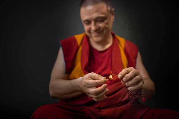Buddyjski mnich trzyma świecę i zapala kadzidełko. - Zdjęcie, obraz