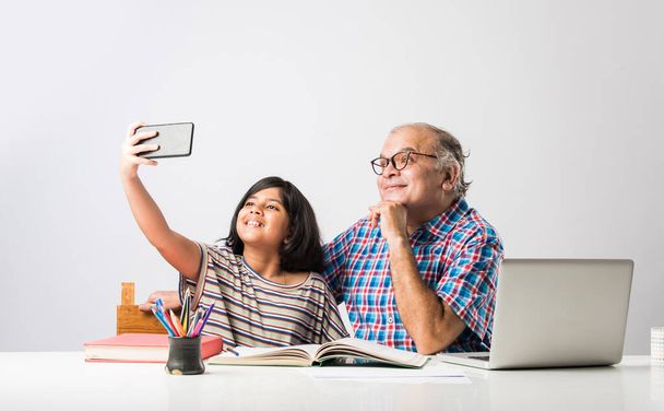 Indian grandfather teaching granddaughter with books, pencil and laptop, home schooling or tuition - Photo, image