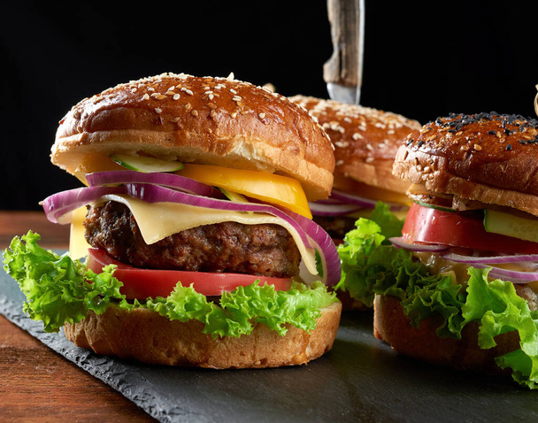 вкусные гамбургеры с котлетами из жареной говядины, помидорами, салатом и луком, хрустящей белой пшеничной мукой с кунжутом. Фаст-фуд  - Фото, изображение