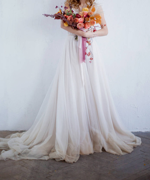 Η νύφη περπατά με όμορφο νυφικό με φθινοπωρινό πολύχρωμο μπουκέτο. Γυναίκα με φθινοπωρινά λουλούδια σε λευκό φόντο - Φωτογραφία, εικόνα