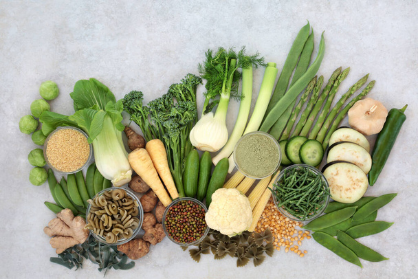Vegane grüne & gelbe Gesundheitsprodukte für die Immunabwehr mit hohen Nährwerten mit Antioxidantien, Mineralstoffen, Vitaminen, Ballaststoffen & intelligenten Kohlenhydraten. Mit Gemüse, Hülsenfrüchten, Nudeln, Getreide und Gewürzen. Flach lag auf grau meliert. - Foto, Bild