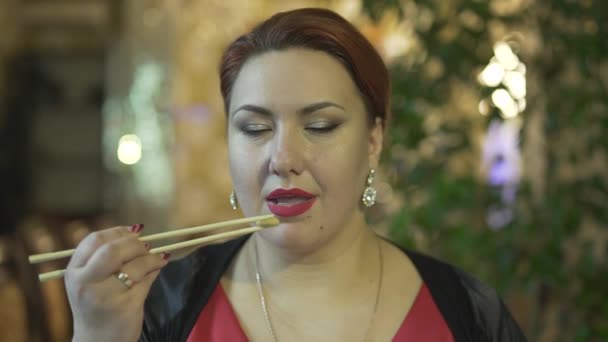 Vista de cerca de la atractiva mujer morena de mediana edad comiendo comida con palillos disfrutando de la comida en un restaurante de lujo - Metraje, vídeo