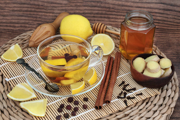 蜂蜜、レモン、シナモン、生姜、クローブ&ホショーソンベリーの熱い飲み物で寒さとインフルエンザのための伝統的なハーブ療法。免疫は治癒のための健康管理を高める。竹、ウィッカーマットと素朴な木で. - 写真・画像