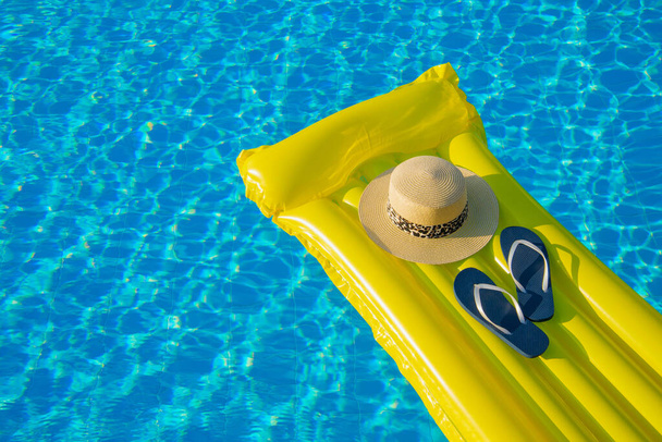 Beach summer holiday background. Inflatable air mattress, flip flops and hat on swimming pool. - Photo, image