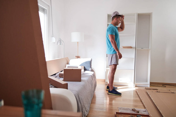 Άνδρας που συναρμολογεί έπιπλα σε νέο διαμέρισμα, μετακομίζει και εργάζεται σκληρά. - Φωτογραφία, εικόνα