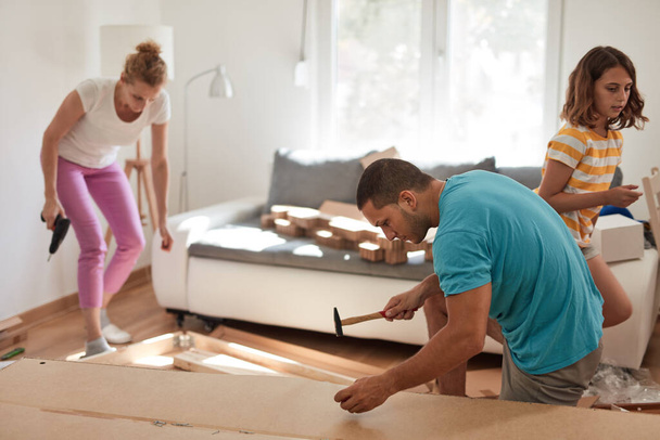 Madre, padre e hija ensamblando muebles en un apartamento nuevo, mudándose y trabajando duro. - Foto, imagen
