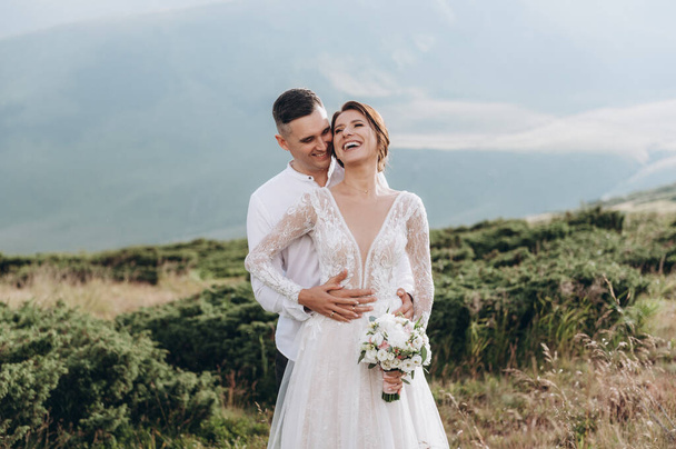 Happy newlyweds smiling, embracing, posing in the mountans - Фото, изображение