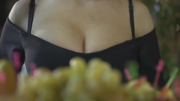Primer plano plano de sexy joven morena seductora mujer en negro escote vestido comiendo frutas de uva solo en restaurante de lujo - Metraje, vídeo