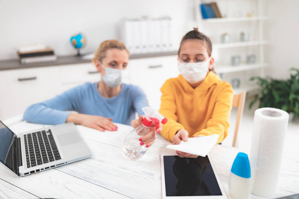 Sterilizing tablet and laptop. Child at home studying education, homeschooling, with private tutor / mother with protective mask in the time of viruses, flu and pandemic. - Photo, Image