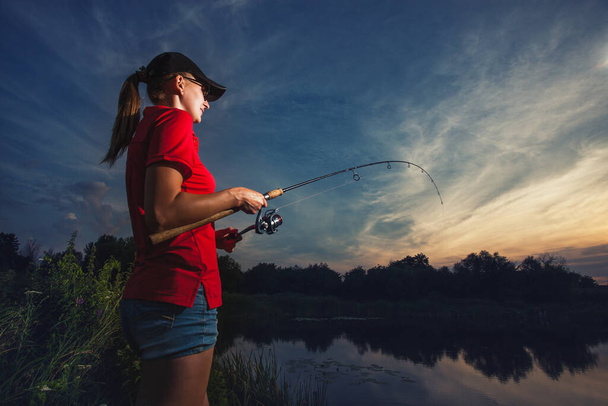 Cute woman is fishing with rod on lake - Фото, зображення