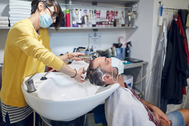 Fryzjer i klient w salonie z maskami medycznymi podczas pandemii wirusowej. Praca z maską bezpieczeństwa. - Zdjęcie, obraz