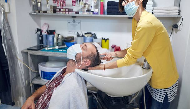 Parrucchiere e cliente in un salone con maschere mediche durante la pandemia virale. Lavorare con maschera di sicurezza. - Foto, immagini