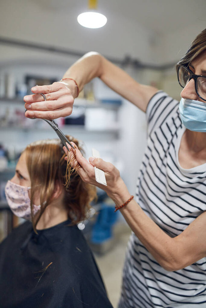 Kapsalon en klant in een salon met medische maskers tijdens viruspandemie. Werken met veiligheidsmasker. - Foto, afbeelding