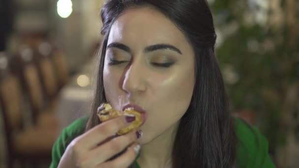 若い女性が近くのレストランで指を舐める汚い手でカスタードペストリーデザートを食べるのを楽しんでいるブルネット - 映像、動画