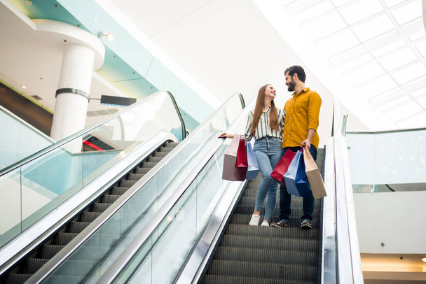 Full length body size rear back behind view of nice attractive cheerful cheery couple visiting fashionable retail store city building standing on escalator spending weekend vacation holiday bargain - 写真・画像