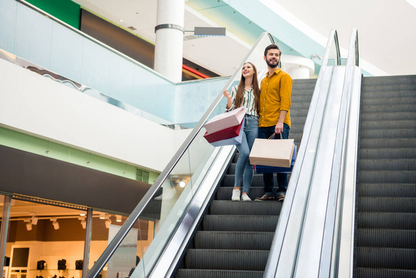 Full size photo of positive comfort cozy man woman move first floor escalator look hold many packages wear striped yellow shirt denim jeans in shopping center mall - Foto, Imagen