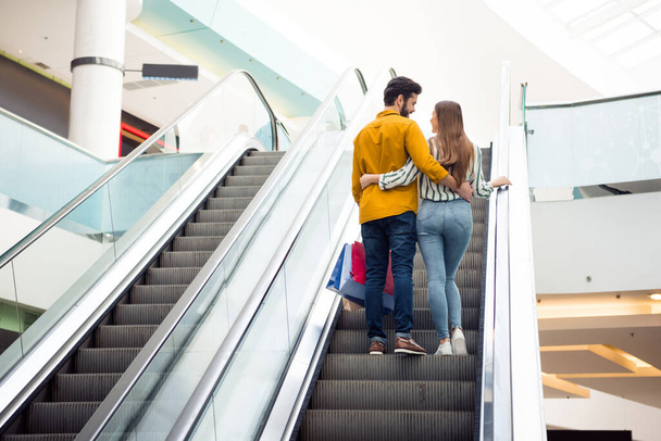 Full body rear behind view photo of attractive lady handsome guy couple spend free time carry bags moving up escalator shopping center hugging wear casual jeans shirt outfit indoors - 写真・画像