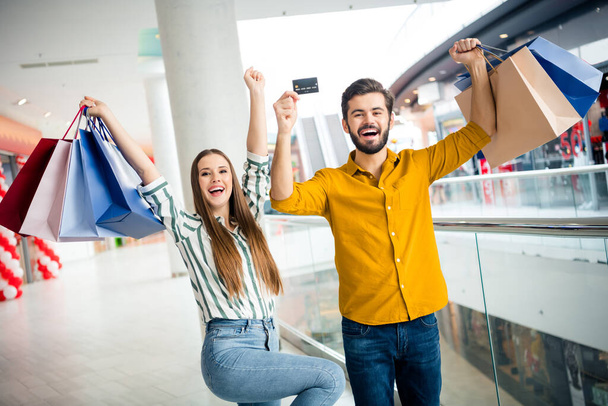 Portrait of positive fun spouses two people man woman win bargain boutique retail lottery pay purchase with credit card raise fists scream yes hold many bags in shopping mall center - Foto, Imagem