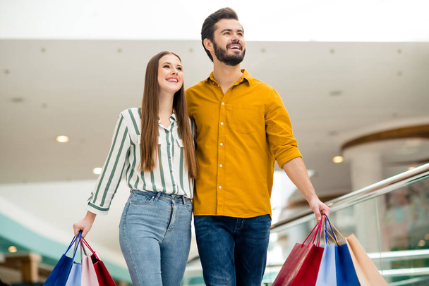 Portrait of positive cheerful spouses man woman wife husband have enjoy fun free time in shopping center mall hold many packages bags wear striped yellow shirt denim jeans - 写真・画像