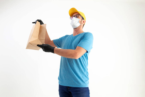 Repartidor con máscara protectora sosteniendo bolsa de papel con comestibles. - Foto, imagen