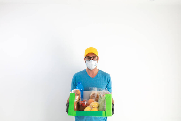 Auslieferer mit Schutzmaske hält Box mit Lebensmitteln. - Foto, Bild