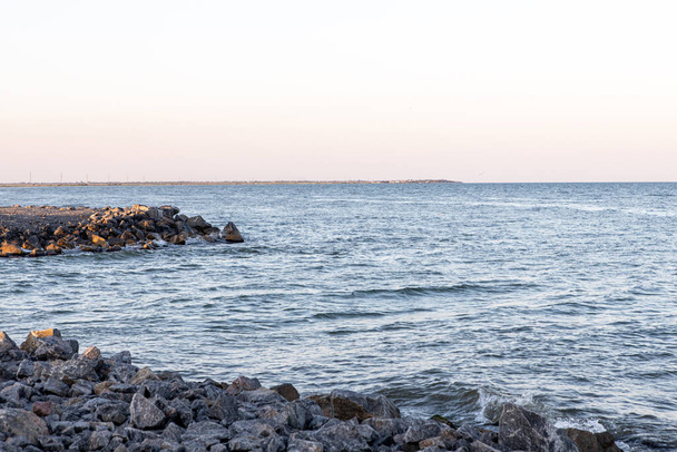 кам'яний і піщаний берег з хвилями під час заходу сонця
 - Фото, зображення