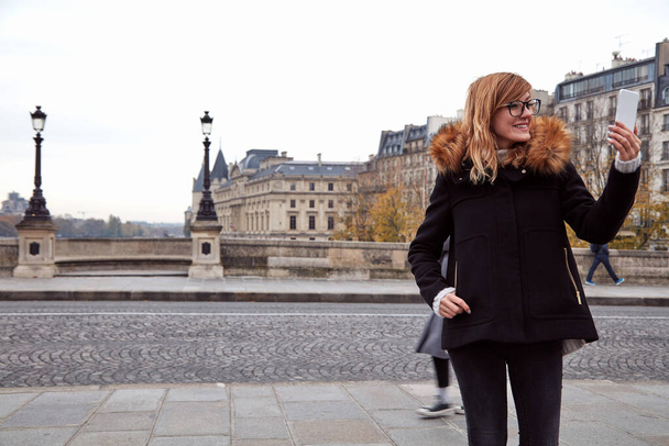 Девушка с мобильным телефоном на фоне Парижа, река Сена в осенний сезон. - Фото, изображение