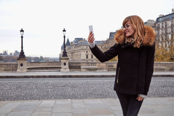 Κορίτσι που χρησιμοποιεί κινητό τηλέφωνο με φόντο την πόλη του Παρισιού, Σηκουάνα ποταμού το φθινόπωρο εποχή. - Φωτογραφία, εικόνα